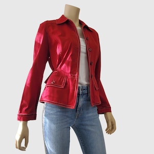 May include: A red jacket with a button-up front, two front pockets, and white stitching. The jacket is paired with blue jeans. The jacket has a collar and long sleeves. The model is wearing a white shirt underneath the jacket.