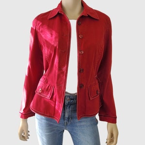 May include: A red jacket with a button-up front, collar, and two front pockets. The jacket has white stitching details and is worn over a white top and blue jeans. The jacket is displayed on a mannequin.