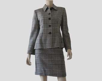 May include: A two-piece suit comprising a blazer and a matching skirt in a black and white houndstooth and plaid pattern. The blazer features a collared neckline, long sleeves, and a front button fastening. The skirt is a knee-length, straight-cut design.