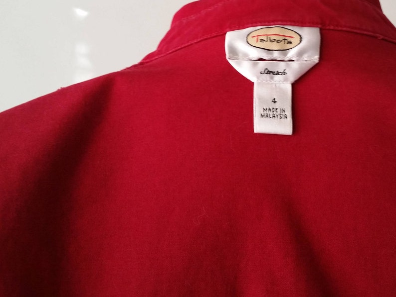 May include: A close-up of a red garment with a white label. The label features the brand name "Talbots" and the word "Stretch". Below the brand name, the label indicates size "4" and "MADE IN MALAYSIA".