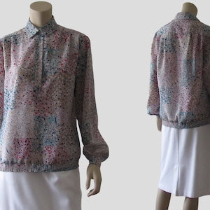 May include: A long-sleeved blouse with a colorful abstract print. The blouse has a collared neckline and a button closure. The fabric is sheer and has a slightly gathered look at the wrists and bottom.