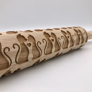 May include: A wooden rolling pin with a repeating pattern of cats with hearts. The rolling pin is made of natural wood and has a smooth, polished finish.