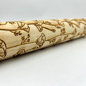 May include: A wooden rolling pin with a floral design. The design features a repeating pattern of stylized flowers and leaves.