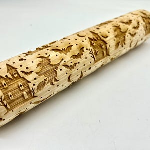 May include: A light-colored wooden rolling pin with a Halloween-themed design. The pin features engraved images of a haunted house, bats, a witch on a broom, and crescent moons. The pin is approximately 16 inches long.
