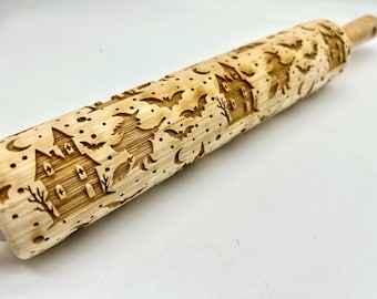 May include: A light-colored wooden rolling pin with a Halloween-themed design. The pin features engraved images of a haunted house, bats, a witch on a broom, and crescent moons. The pin is approximately 16 inches long.