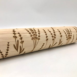 May include: A wooden rolling pin with a lavender floral design engraved on the surface. The rolling pin is made of natural wood and has a light brown color.