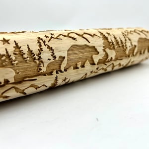 May include: A wooden rolling pin with a carved design of bears and trees. The rolling pin is made of light wood and has a natural finish.