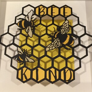 May include: Black paper cut-out of a honeycomb with three bees and the words "Be Kind" in yellow.