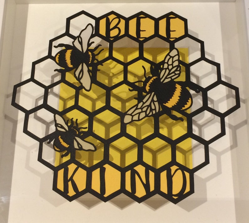 May include: Black paper cut-out of a honeycomb with three bees and the words "Be Kind" in yellow.