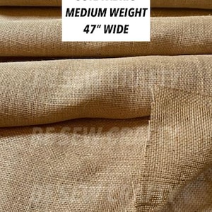 May include: A roll of natural tan burlap jute fabric with a visible woven texture. The fabric is medium weight and 47 inches wide. Text on the image reads: NATURAL BURLAP JUTE FABRIC MEDIUM WEIGHT 47 INCHES WIDE, and BE SEW CRAFTY ETSY.COM/BESEWCRAFTY.