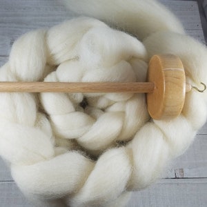 May include: A wooden spinning wheel with a white wool roving. The wheel has a wooden spindle and a wooden whorl. The whorl has a metal hook.