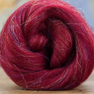 Puede incluir: Primer plano de una lana cardada de color rojo intenso con un ligero brillo. La lana cardada está bien compacta y tiene una textura suave y esponjosa.