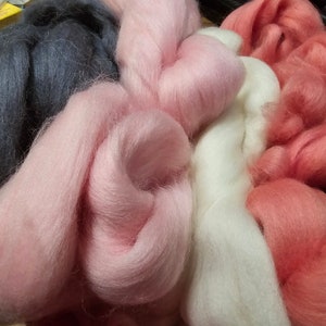 May include: A collection of soft, fluffy yarn in shades of pink, white, and gray. The yarn is arranged in a loose pile, with the different colors blending together.