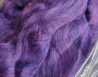 Puede incluir: Primer plano de una fibra morada y azul, probablemente lana o alpaca, en una bolsa de plástico. La fibra es suave y esponjosa, y parece estar teñida a mano.