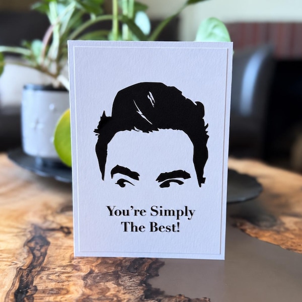 Könnte beinhalten: Eine weiße, rechteckige Grußkarte mit einer schwarzen Silhouetten-Illustration von Haaren und Augenbrauen einer Person. Unter der Illustration ist der Text "You're Simply The Best!" in einer schwarzen Serifenschrift aufgedruckt.