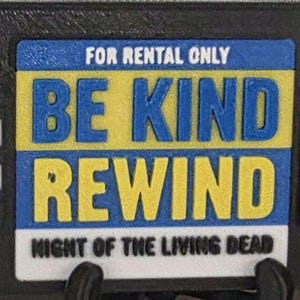 May include: A black VHS tape with a blue and yellow label that reads "FOR RENTAL ONLY BE KIND REWIND NIGHT OF THE LIVING DEAD." The tape has white and black reel details and the VHS logo.