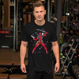 K&ouml;nnte beinhalten: Schwarzes T-Shirt mit einem Grafikdruck von Deadpool in Kampfpose mit Schwertern und Pistolen. Der Hintergrund ist schwarz mit wei&szlig;en Blitzen.