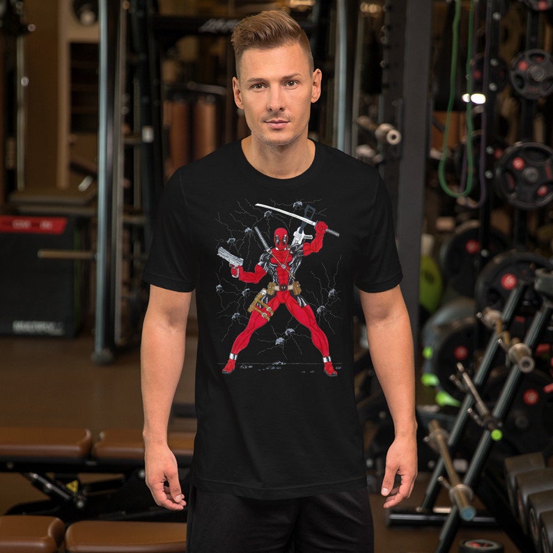 K&ouml;nnte beinhalten: Schwarzes T-Shirt mit einem Grafikdruck von Deadpool in Kampfpose mit Schwertern und Pistolen. Der Hintergrund ist schwarz mit wei&szlig;en Blitzen.