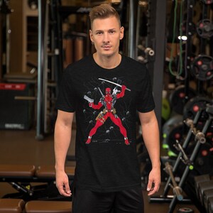 K&ouml;nnte beinhalten: Ein schwarzes T-Shirt mit einem Grafikdruck von Deadpool in einem rot-schwarzen Anzug, der ein Katana und zwei Pistolen h&auml;lt. Die Grafik ist von einem schwarz-wei&szlig;en Blitzmuster umgeben.