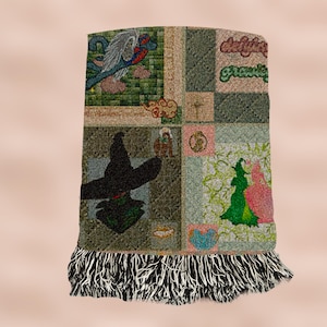 Könnte beinhalten: Eine mehrfarbige gewebte Wolldecke mit Patchwork-Muster, das eine Hexe, einen Vogel und eine Wolke zeigt. Die Decke hat schwarze und weiße Fransen an den Rändern.