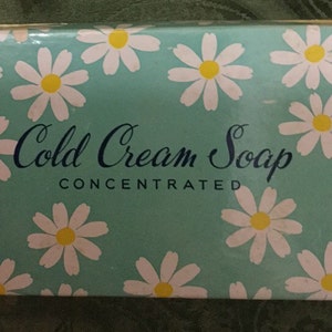 May include: A rectangular box of Cold Cream Soap, with a light teal background and a pattern of white daisies with yellow centers. The words "Cold Cream Soap" are written in a cursive font, with "Concentrated" below.