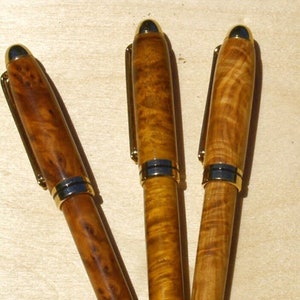 May include: Three wooden pens with gold accents and a wood grain pattern. The pens are arranged in a V-shape.