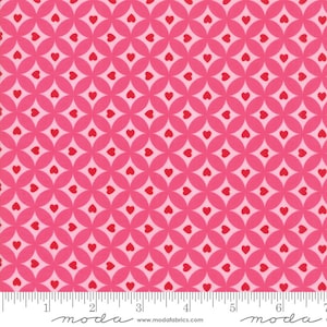 以下が含まれることがあります： 赤いハートが円形に並んだパターンが繰り返されるピンク色の生地。生地には「moda」という文字が印刷された白い定規があります。