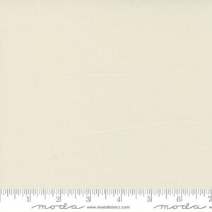 May include: A solid off-white fabric with a subtle texture. The fabric is shown with a ruler for scale.