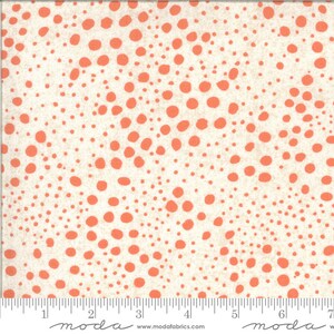 May include: White fabric with a repeating pattern of coral-coloured dots of varying sizes. The fabric is textured and has a subtle sheen. The fabric is measured in inches with the text "moda" printed on the ruler.
