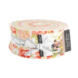 Może przedstawiać: Rolka preciętej tkaniny Moda Fabrics z nadrukiem kwiatowym z różowymi, czerwonymi i żółtymi kwiatami na białym tle. Rolka jest związana białą wstążką z nadrukowanym słowem "moda". Etykieta na rolce głosi "Moda Fabrics - Supplies".