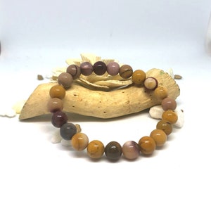 May include: A bracelet made of brown, yellow, and purple gemstone beads. The bracelet is on a piece of driftwood.