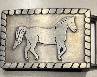 May include: Silver belt buckle with a horse silhouette design. The buckle has a rope-like border.