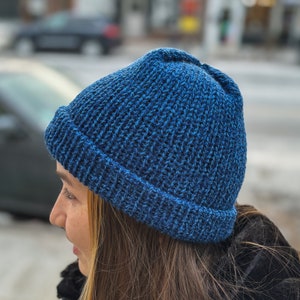 May include: A person wearing a blue knitted beanie hat. The hat has a ribbed texture and a folded brim.