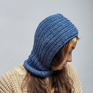 May include: A blue knitted hooded scarf with a ribbed texture. The scarf is worn by a person with long brown hair.