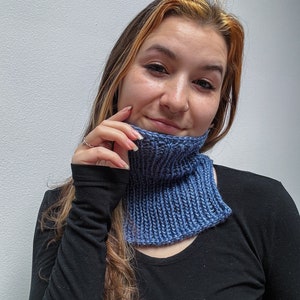 May include: A woman wearing a black long-sleeved shirt with a blue knitted cowl neck scarf. The scarf is a gradient of blue shades.