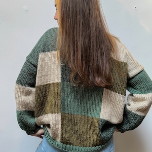 May include: A green, brown, and beige checkered sweater with long sleeves. The sweater is made of a soft, knitted fabric.
