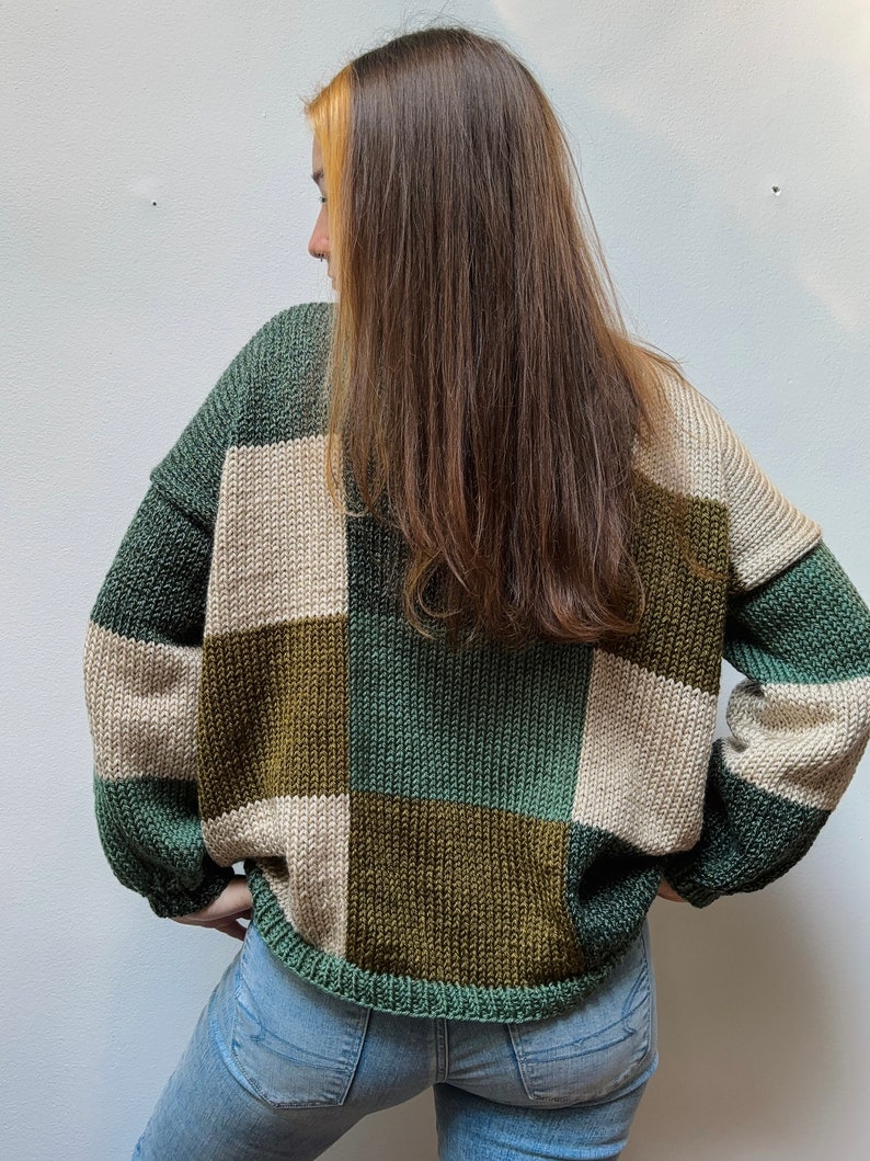 May include: A green, brown, and beige checkered sweater with long sleeves. The sweater is made of a soft, knitted fabric.