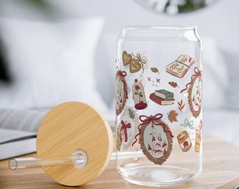May include: A clear glass can-shaped tumbler with a bamboo lid and straw. The tumbler is decorated with illustrations of a rose, books, and a castle. The lid is round and made of light-colored wood.
