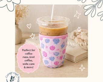 May include: A pink drink sleeve with a floral pattern, holding an iced coffee with a straw. The sleeve has blue and pink floral designs and the text "Perfect for coffee runs, iced coffee, soda cans & more!"