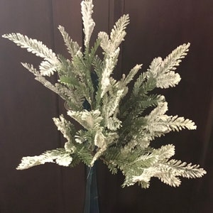 May include: A frosted artificial evergreen sprig with green leaves and white tips. The sprig is perfect for adding a touch of winter to your home decor.