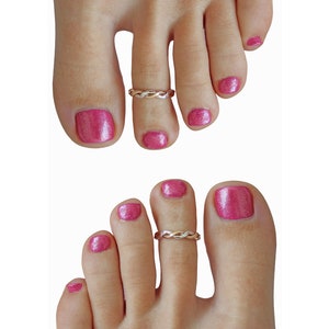 May include: Two feet with pink nail polish and a silver and gold braided toe ring on the second toe of each foot.