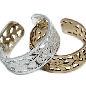 May include: Two silver and gold toe rings with a floral design. The rings are open and have a delicate, intricate design.