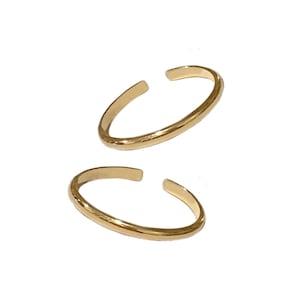 May include: Two gold ear cuffs, each with a simple, rounded shape. The cuffs are made of a smooth, shiny metal.