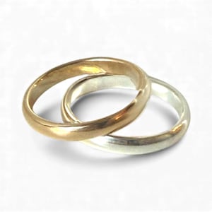 May include: Two intertwined rings, one gold-toned and the other silver-toned, are displayed against a white background. The rings are smooth and simple in design, with a classic, elegant appearance. The gold ring appears to be slightly thicker than the silver ring.