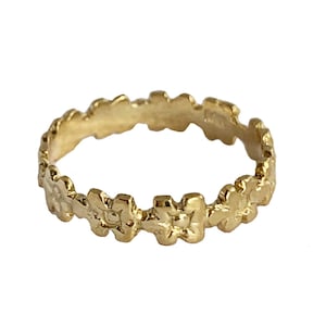 May include: A gold ring with a delicate floral design. The ring is made of a smooth, polished metal and features a repeating pattern of small flowers.
