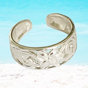May include: Silver toe ring with a floral design. The ring is adjustable and has a delicate, intricate pattern.