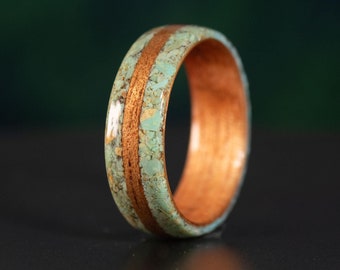 May include: A ring featuring a central band of brown wood flanked by two sections of light blue, speckled turquoise-colored inlay. The interior of the ring is lined with smooth brown wood, and the entire surface has a polished, glossy finish.