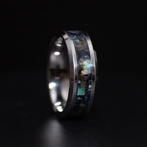 May include: A silver ring with a black and iridescent inlay. The inlay is made of abalone shell and has a unique pattern.
