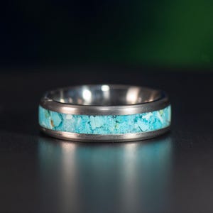 May include: A silver ring with a turquoise inlay. The ring is a simple band with a thin line of turquoise set into the metal.