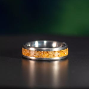 May include: A silver ring with a band of embedded orange sand.